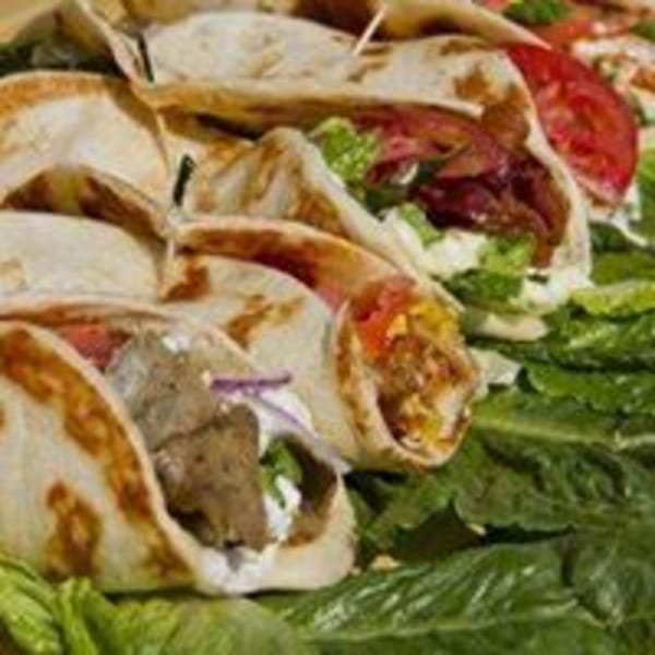 Several Pita Place gyros and wraps with meat, lettuce, tomatoes, and sauce on a bed of lettuce.