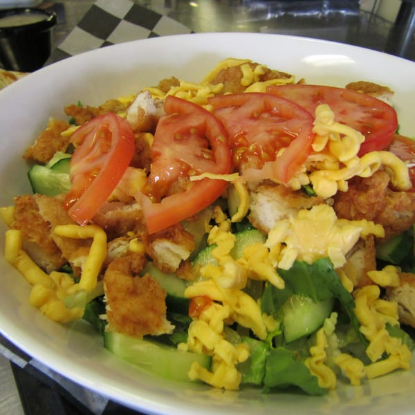 A Pita Place Greek salad with crispy chicken, tomatoes, cucumbers, and shredded cheese.