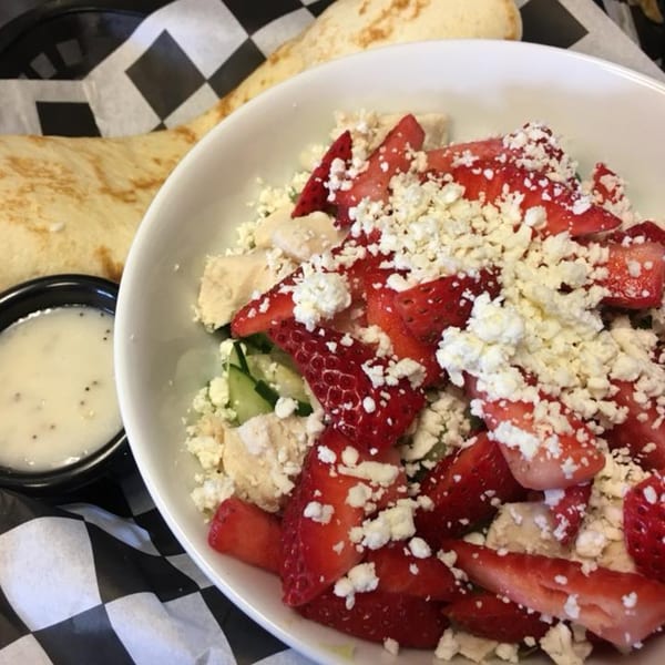 Pita Place Greek salad with strawberries, feta, chicken, cucumbers, and dressing, served with pita bread.