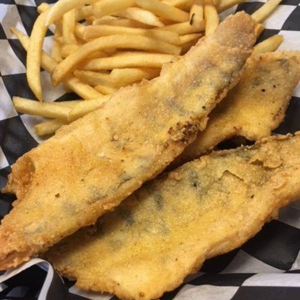 Fried fish fillets and french fries served in a black and white checkered paper basket.