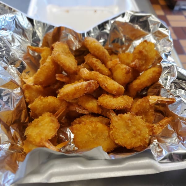 Golden-brown fried shrimp with tails on, served in a foil-lined takeout container.